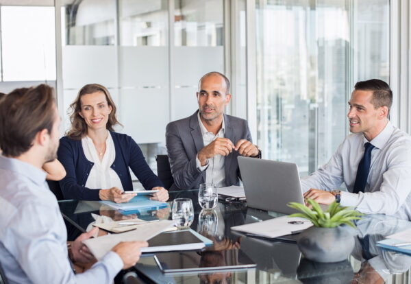 Multiethnic group of business people sitting in annual meeting in conference room. Mature leader with businessmen and businesswomen discussing. Busy partners working together in modern office.
